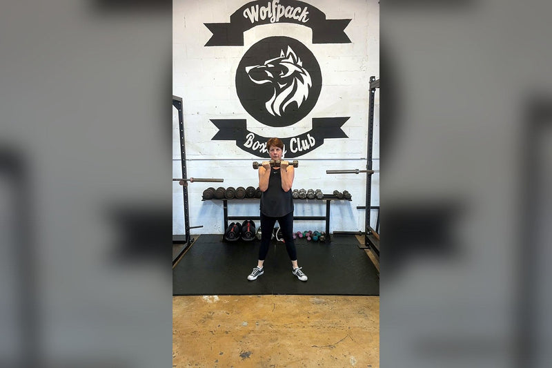 Maria strength training in front of the Wolfpack Boxing Club logo wall